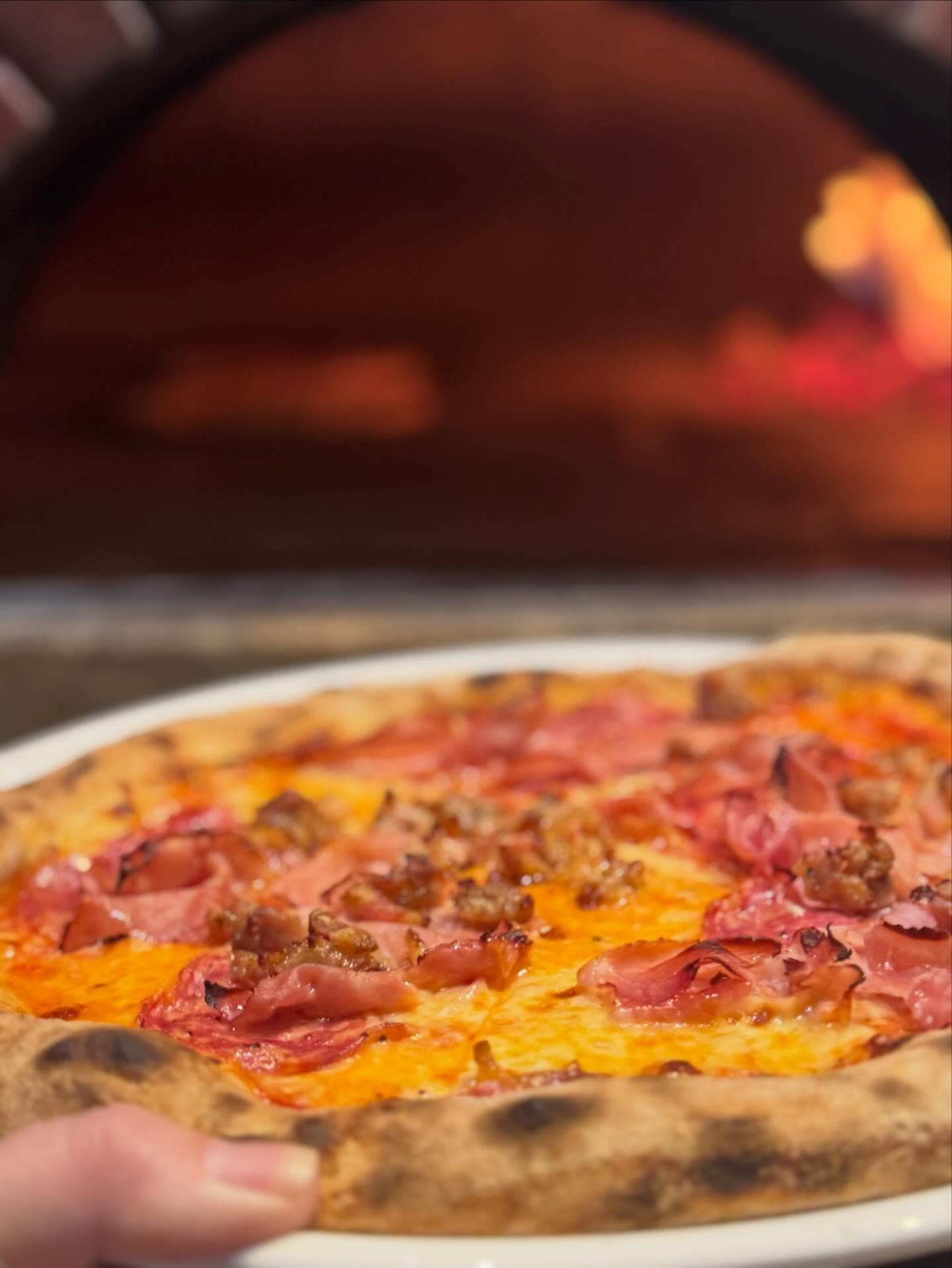 A woodfired pizza held up in front of the oven fire at La Cucina